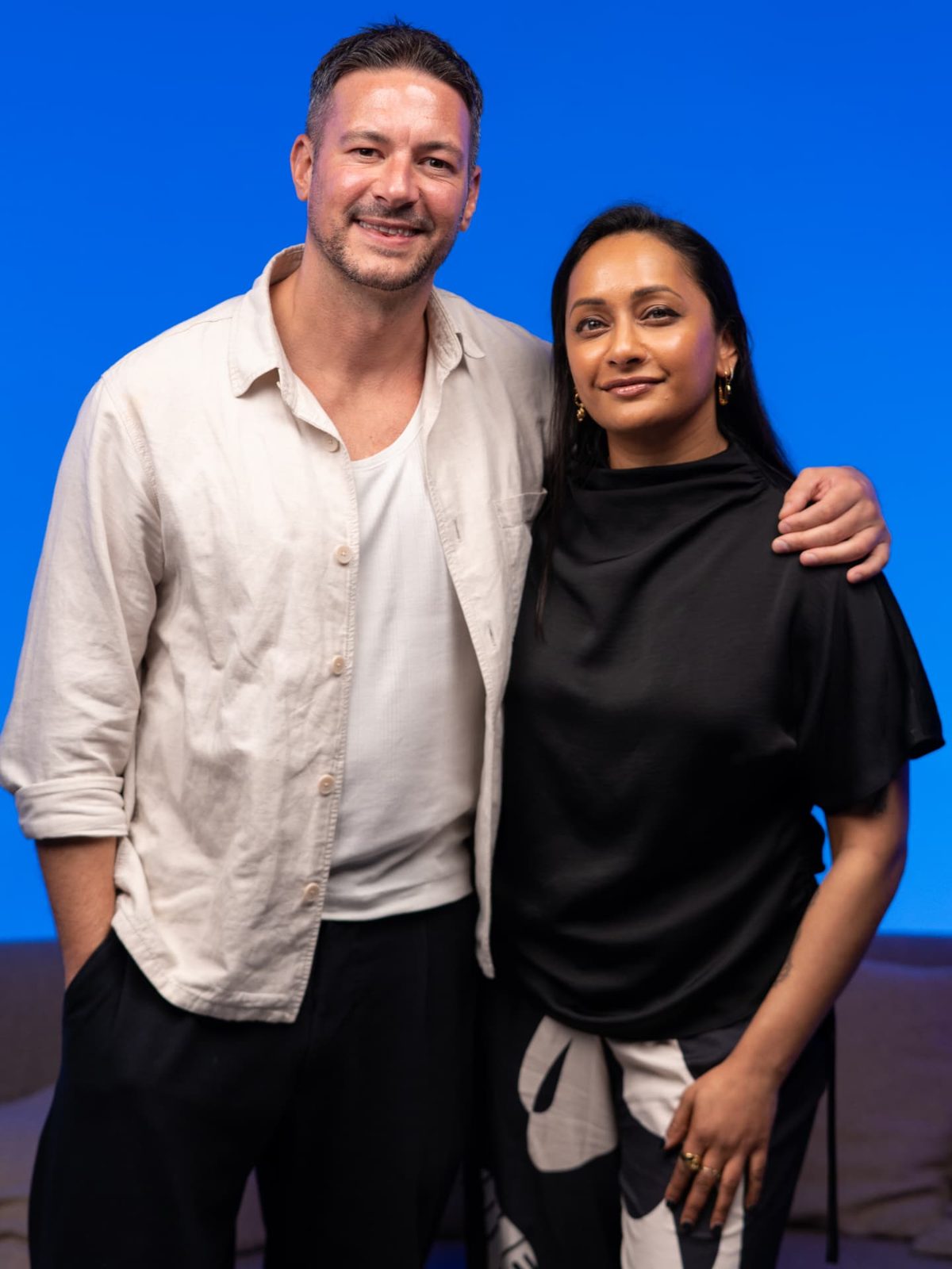 Two hosts photographed together on a blue studio backdrop