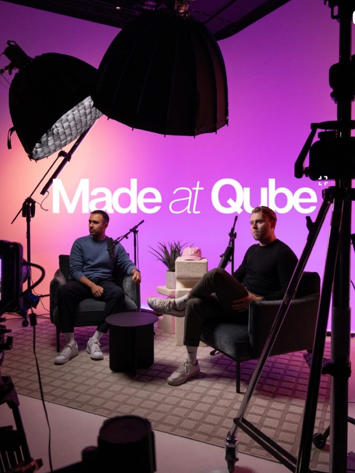 Two hosts recording on a magenta-lit branded studio set
