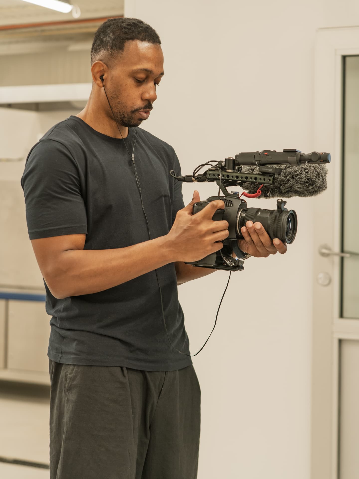 Operator setting up a shoulder-rigged camera with shotgun mic in a facility corridor