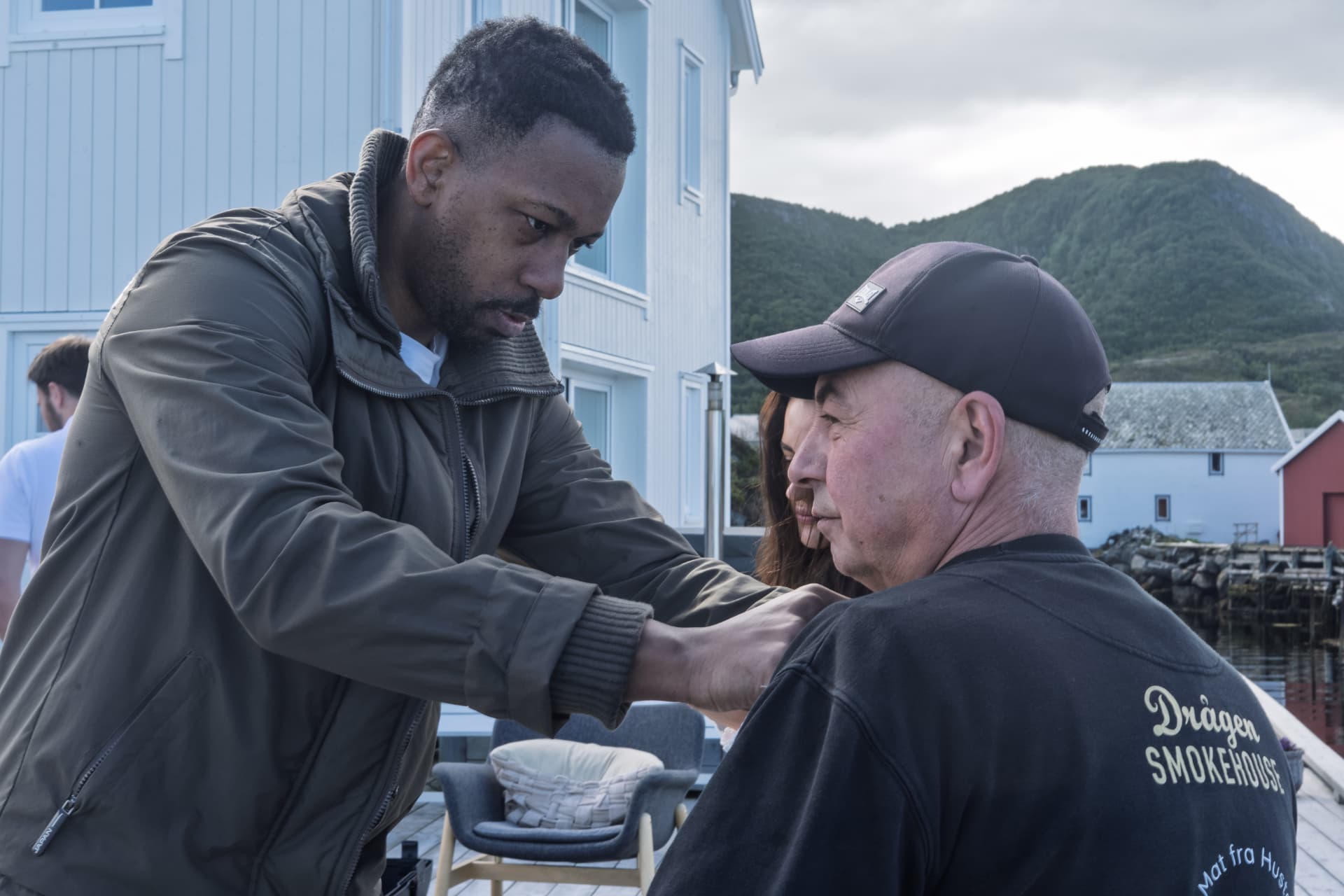 Producer fitting a lapel mic to a guest on a jetty outside a Norwegian smokehouse